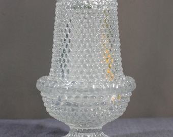 May include: A clear glass vase featuring a textured hobnail pattern across its surface. The vessel has a tapered cylindrical body that widens into a rounded base, supported by a short, fluted pedestal foot with a scalloped edge at the bottom.