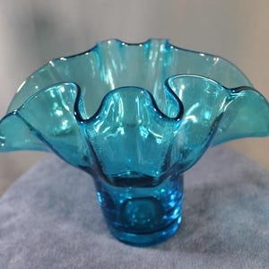 May include: A turquoise glass bowl with a ruffled rim. The bowl has a wide, open design with a textured base. The glass is a vibrant shade of blue-green, and the ruffled edge adds a decorative touch. This bowl is suitable for decorative purposes.