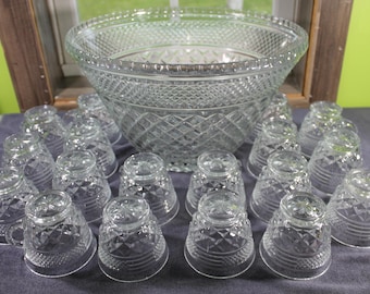 May include: A large clear glass punch bowl and a set of matching punch cups, all featuring a pressed diamond pattern and a textured base. The set includes one wide-rimmed bowl and multiple small handled cups arranged in front of the bowl.