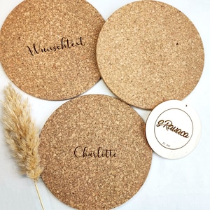 May include: Three round cork coasters with a natural brown color. The coasters have a smooth surface and are engraved with the text "Wunschtext", "Charlotte", and "g Rauaca Est. 2020".
