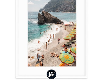 May include: A beach scene with a rocky cliff, turquoise water, and colorful striped umbrellas. People are swimming and relaxing on the beach.