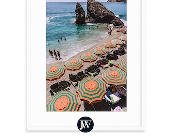 May include: A beach scene with colorful striped umbrellas and lounge chairs on a sandy beach. The beach is bordered by a rocky cliff and the ocean is a bright blue.