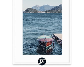 May include: A wooden boat with a green stripe is docked at a pier on a calm lake. The boat is facing the camera and the lake is surrounded by mountains in the distance.