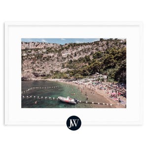 May include: An aerial view of a rocky coastline with a small boat in the water. The water is clear and blue, and there are people swimming and sunbathing on the beach.