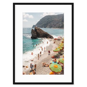 May include: A beach scene with colourful striped umbrellas and people swimming and sunbathing on a sandy beach with a rocky cliff in the background.
