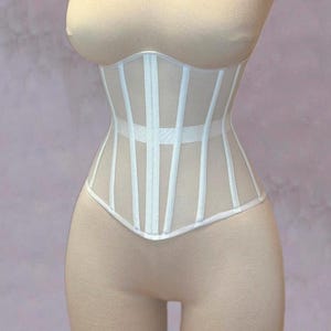 May include: White mesh corset with boning and a zipper closure. The corset is on a dress form.