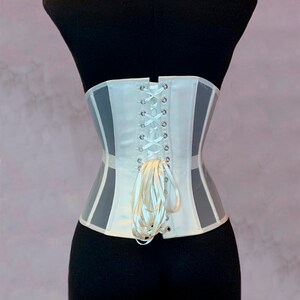 May include: White corset with a lace-up back and a satin ribbon. The corset has a sheer panel on the sides.
