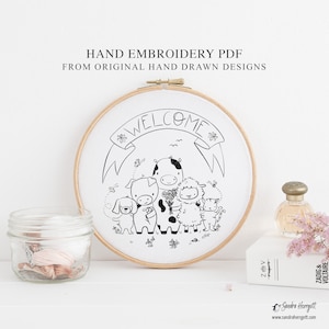 Op de afbeelding: Een handborduur-PDF met een zwart-wit ontwerp van cartoon dieren, waaronder een koe, een varken, een schaap en een hond, onder een banner met de tekst "WELCOME". Het ontwerp zit in een houten borduurring. De tekst op de afbeelding luidt "HAND EMBROIDERY PDF FROM ORIGINAL HAND DRAWN DESIGNS".
