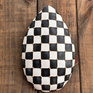 Peut inclure: Un objet décoratif en forme de goutte d'eau avec un motif à carreaux noir et blanc. De petits points dorés sont espacés uniformément sur la surface. L'objet est posé sur un fond en bois.