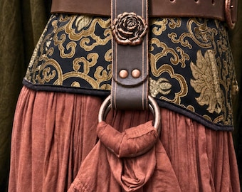 May include: A brown leather belt featuring a vertical strap attachment with a copper-colored rose emblem and a large metal ring. The belt is worn over a black bodice with gold floral patterns and a gathered, solid-colored terracotta-toned skirt.
