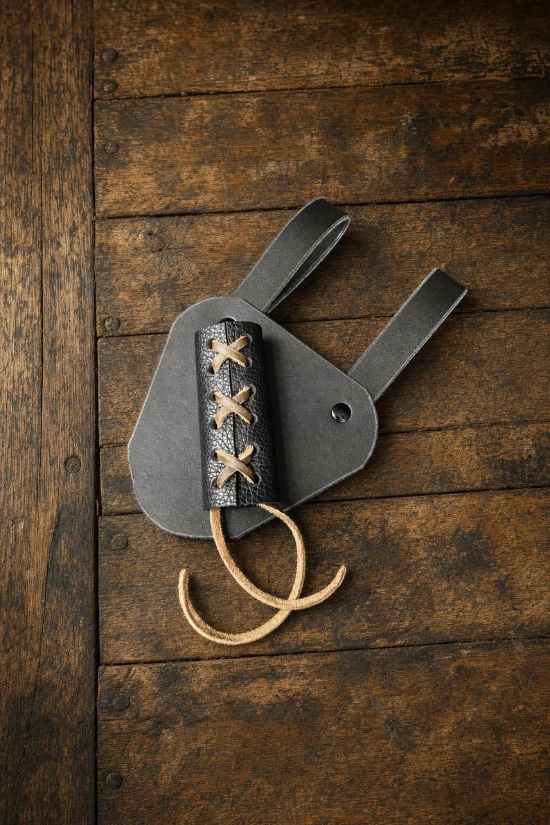 Puede incluir: Un accesorio de cintur&oacute;n de cuero negro con un soporte cil&iacute;ndrico de superficie texturizada. El soporte est&aacute; asegurado con cordones de cuero color canela en un patr&oacute;n entrecruzado e incluye dos largos lazos de cuero colgando del borde.