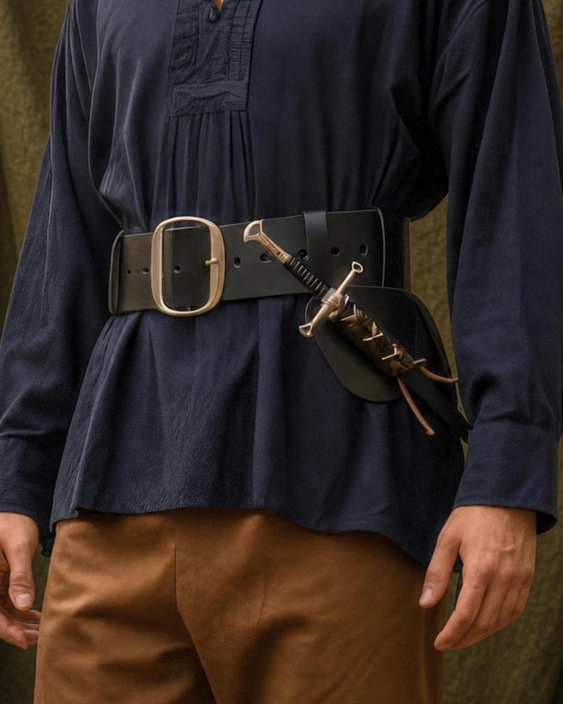 Puede incluir: Un cintur&oacute;n ancho de cuero negro con una gran hebilla met&aacute;lica ovalada y una funda de cuero marr&oacute;n oscuro que sostiene una peque&ntilde;a daga de metal con mango negro. El cintur&oacute;n se lleva sobre una camisa azul oscuro y pantalones marrones.