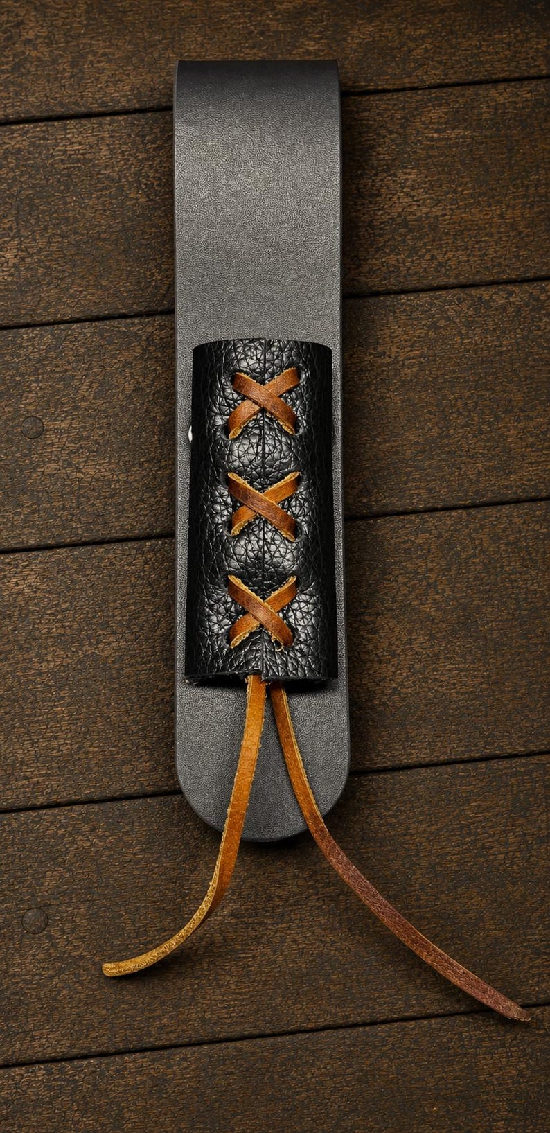 May include: A black leather sheath featuring a textured black leather overlay secured with brown leather lacing in a crisscross pattern. The lacing extends from the bottom of the overlay in two long, loose brown leather cords.