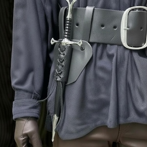 May include: A silver and black sword in a black leather sheath attached to a wide black belt with a silver buckle. The sword has a detailed hilt and a pointed blade. The sheath is laced with black cord.
