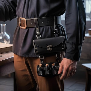 Könnte beinhalten: Schwarzer Ledergürtel mit passendem Beutel und einem unteren Fach mit kleinen Glasfläschchen. Der Gürtel hat eine große Schnalle und wird mit einem dunklen Hemd und braunen Hosen getragen. Der Beutel hat einen dekorativen Verschluss.