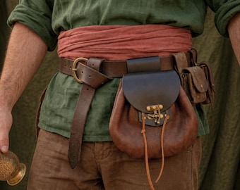 May include: A dark brown leather belt featuring a brass buckle and a large, rounded leather pouch with a dark flap and brass latch closure. The pouch is attached to the belt alongside a smaller, rectangular leather accessory bag.