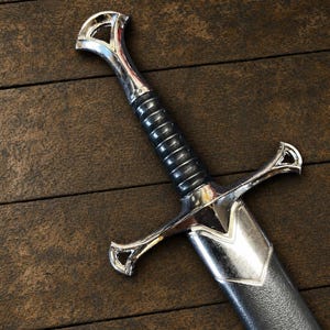 May include: A sword with a polished silver-tone metal pommel, crossguard, and throat. The handle features a black, ribbed grip. The sword is partially encased in a black, textured scabbard with a silver-tone metal fitting at the top.