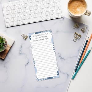May include: A lined notepad with the text "Things I Want to Tell Him But He's in Airplane Mode Again" in a white and blue design. The notepad is on a marble-patterned desk with a keyboard, coffee cup, and pencils.