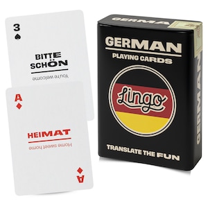 May include: A black metal tin labelled GERMAN PLAYING CARDS and TRANSLATE THE FUN with a circular German flag graphic and the word Lingo. Two white playing cards are shown: one with a spade, 3, and BITTE SCHÖN, and one with a diamond, A, and HEIMAT.