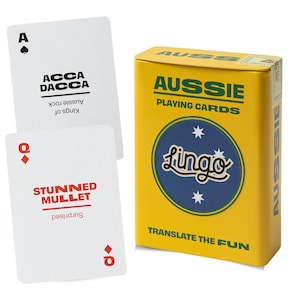 Puede incluir: Una caja rectangular amarilla etiquetada como Aussie Playing Cards con un logotipo circular azul y el texto Translate the Fun. Se muestran dos cartas blancas, una con el As de picas con Acca Dacca y la Reina de diamantes con Stunned Mullet.