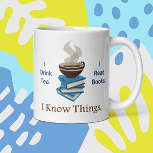 May include: White ceramic mug with a brown and blue illustration of a cup of tea on top of a stack of books. The text "I Drink Tea. I Read Books. I Know Things." is printed on the mug.