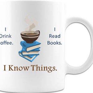 May include: White ceramic mug with a brown coffee cup with steam coming out of it, sitting on top of a stack of blue books. The mug has the text "I Drink Coffee. I Read Books. I Know Things."