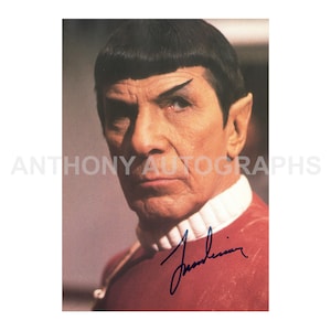 Peut inclure: Portrait d'un homme aux cheveux noirs, aux oreilles pointues et à la forme de sourcils distinctive. Il porte un uniforme rouge avec un col blanc. L'image comprend une signature et le texte "ANTHONY AUTOGRAPHS".