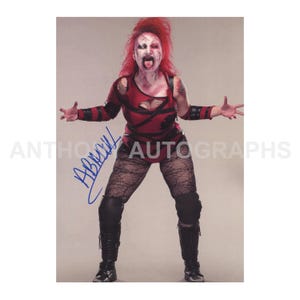 May include: A professional wrestler in a red and black costume with matching makeup and red hair. The wrestler is wearing black boots, knee pads, and fishnet stockings. The image includes a signature in blue ink.