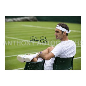 May include: A photograph featuring a tennis player in a white shirt, shorts, and headband, seated in a green chair on a tennis court. The player's signature is visible. The background shows a green lawn.