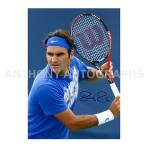 May include: A signed photograph of a tennis player in a blue shirt and headband, holding a Wilson tennis racket. The player is wearing a white wristband with a Nike logo. The background is a solid blue.