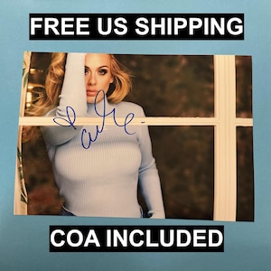 Puede incluir: Fotografía de una persona con un jersey de cuello alto azul claro, con una firma en tinta azul. La imagen está enmarcada por una ventana blanca y el texto "COA INCLUDED" está en la parte inferior.