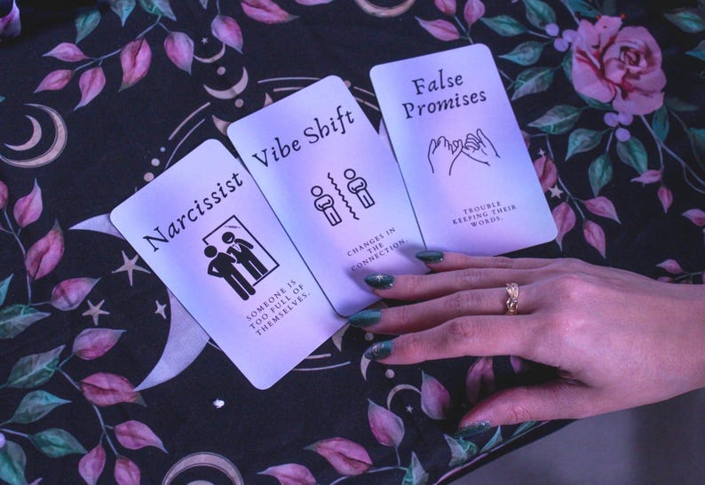 May include: Three tarot cards with the words "Narcissist", "Vibe Shift", and "False Promises". The cards are on a floral patterned cloth. The "Narcissist" card has an image of two people. The "Vibe Shift" card has an image of two figures separated by a line.