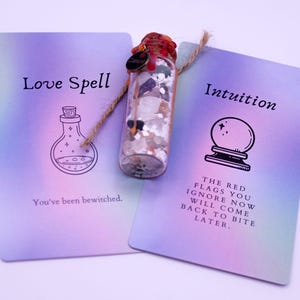 May include: A clear glass bottle filled with crystals and a red stopper, flanked by two cards. One card reads "Love Spell" with a potion bottle illustration and "You've been bewitched." The other card says "Intuition" with a crystal ball illustration and a warning.