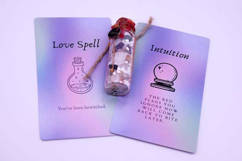 May include: A clear glass bottle filled with crystals and a red stopper, flanked by two cards. One card reads "Love Spell" with a potion bottle illustration and "You've been bewitched." The other card says "Intuition" with a crystal ball illustration and a warning.