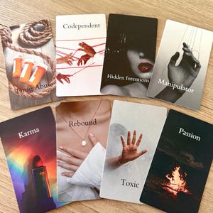 Può includere: Un insieme di carte dei tarocchi con varie immagini e testo. Le carte includono "Drug Abuse", "Codependent", "Hidden Intentions", "Manipulator", "Karma", "Rebound", "Toxic" e "Passion". Le carte sono disposte su una superficie di legno.