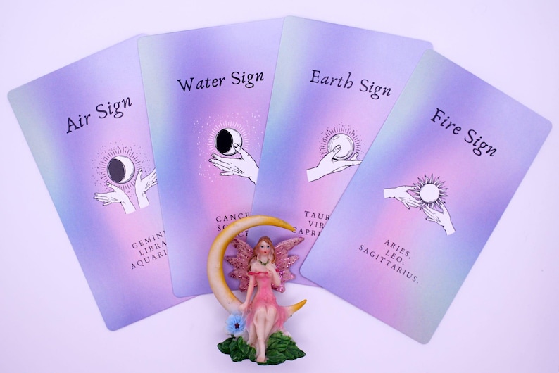 May include: Four tarot cards with pastel purple backgrounds are displayed, each labeled with an astrological element: Air, Water, Earth, and Fire. A fairy figurine sits in front of the cards. The cards feature illustrations of hands holding celestial objects.