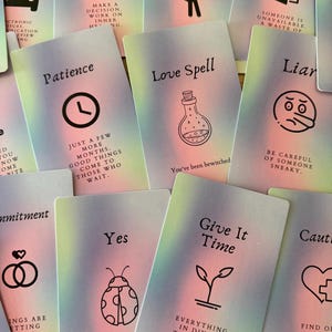 May include: A collection of oracle cards with pastel gradient backgrounds. Each card features a unique illustration and text, including a clock for "Patience" and a potion bottle for "Love Spell". Other cards say "Yes" and "Give it Time".
