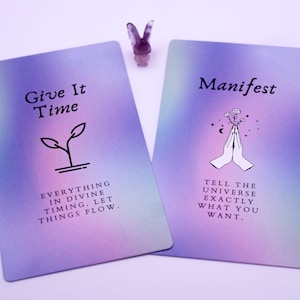 May include: Two tarot cards with a purple and pink gradient background. One card reads "Give It Time" with a plant graphic and the text "Everything in divine timing. Let things flow." The other card says "Manifest" with hands and flowers and the text "Tell the universe exactly what you want."