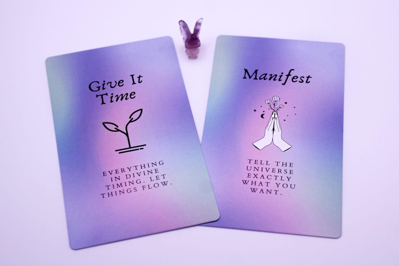 May include: Two tarot cards with a purple and pink gradient background. One card reads "Give It Time" with a plant graphic and the text "Everything in divine timing. Let things flow." The other card says "Manifest" with hands and flowers and the text "Tell the universe exactly what you want."