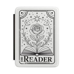 May include: A white e-reader case featuring a black line art illustration of an open book with a rose growing from the pages. Above the rose are crescent moons and stars. The text THE READER is printed in black at the bottom of the rectangular cover.