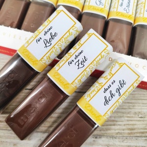 May include: Assortment of small chocolate bars wrapped in clear plastic with yellow and white labels. The labels have the word "Danke" and various German phrases, including "f&uuml;r deine Liebe", "f&uuml;r deine Zeit", and "dass es dich gibt".