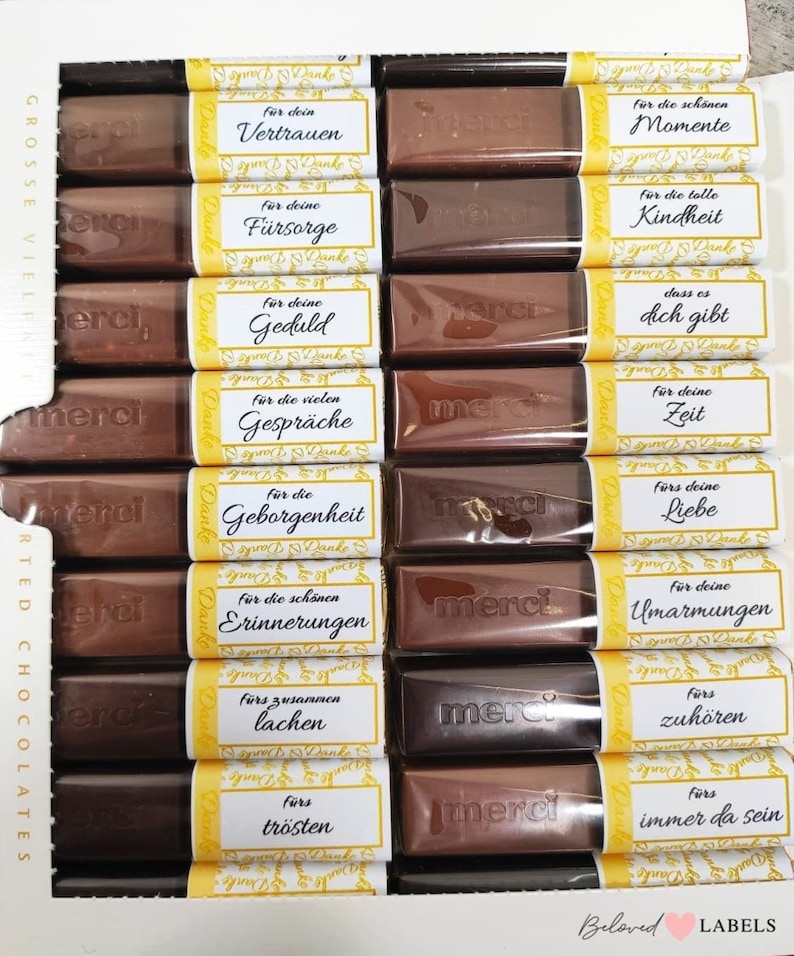 May include: A box of chocolate bars with yellow and white labels. Each label has a different message of thanks in German. The messages include "Vertrauen", "F&uuml;rsorge", "Geduld", "Gespr&auml;che", "Geborgenheit", "Erinnerungen", "Lachen", "Tr&ouml;sten", "Momente", "Kindheit", "Dich gibt", "Zeit", "Liebe", "Umarmungen", "Zuh&ouml;ren", "Immer da sein".
