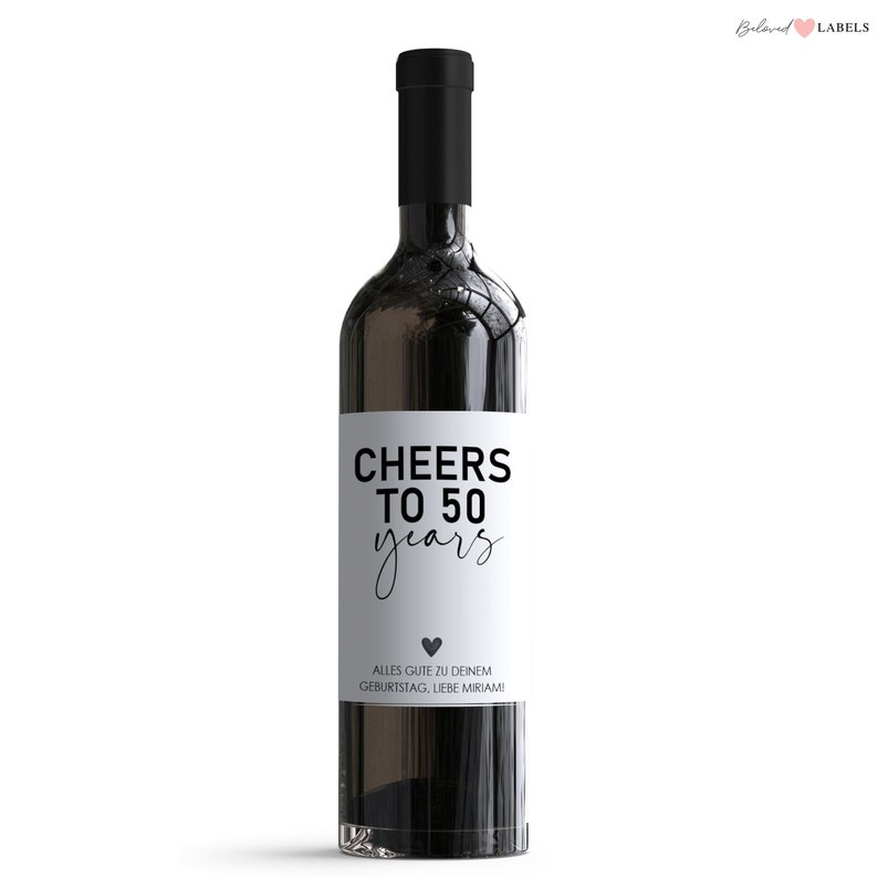 May include: A white wine bottle label with black text that reads "Cheers to 50 years" and "Alles Gute zu deinem Geburtstag, Liebe Miriam!" with a small black heart.