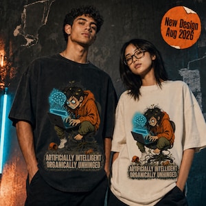 May include: Two oversized t-shirts, one black and one cream, each featuring a graphic of a person in an orange hoodie using a laptop with a glowing blue brain icon above it. The text reads: ARTIFICIALLY INTELLIGENT ORGANICALLY UNHINGED.