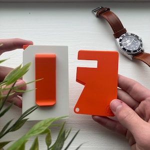 Puede incluir: Dos herramientas de plástico naranja, una con un clip y la otra con un diseño multiherramienta. Las herramientas están sobre un fondo blanco.