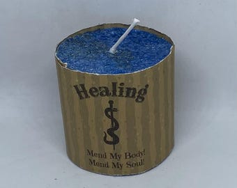 May include: A blue candle with a brown label that reads "Healing" with a caduceus symbol and the text "Mend My Body! Mend My Soul!"