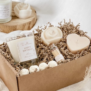 Op de afbeelding: Een bruine kartonnen cadeaudoos gevuld met verschillende kaarsen. De doos bevat een heldere glazen kaars met de tekst "To Mum Happy Birthday Love Ola & Sam", een hartvormige kaars, een roosvormige kaars en een klein glazen potje met lucifers.