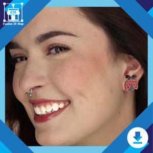 May include: A close-up of a person's face with a small red and black ladybug earring in their right ear. The person is smiling and has a nose ring.