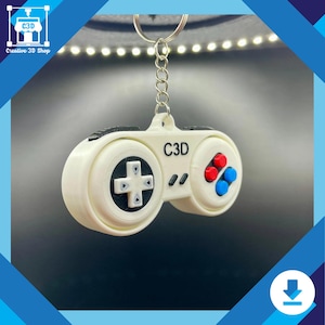 May include: White plastic keychain shaped like a retro video game controller with black buttons and red and blue accents. The keychain has the text "C3D" printed on it.