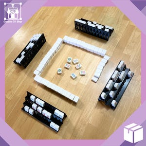 May include: A set of black plastic mahjong racks with white tiles. The tiles are arranged in a square shape with a few tiles scattered in the center. The tiles have Chinese characters and symbols on them.